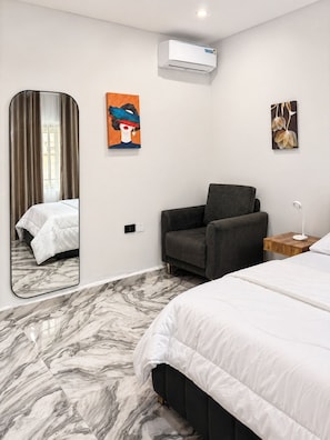 A hotel room with a bed, a chair, a mirror, and artwork on the walls.