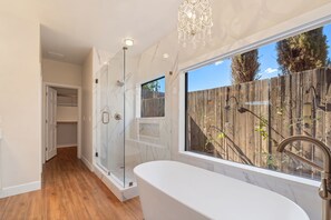 Une salle de bain avec une douche en verre, une baignoire et une fenĂȘtre donnant sur une clĂŽture en bois.