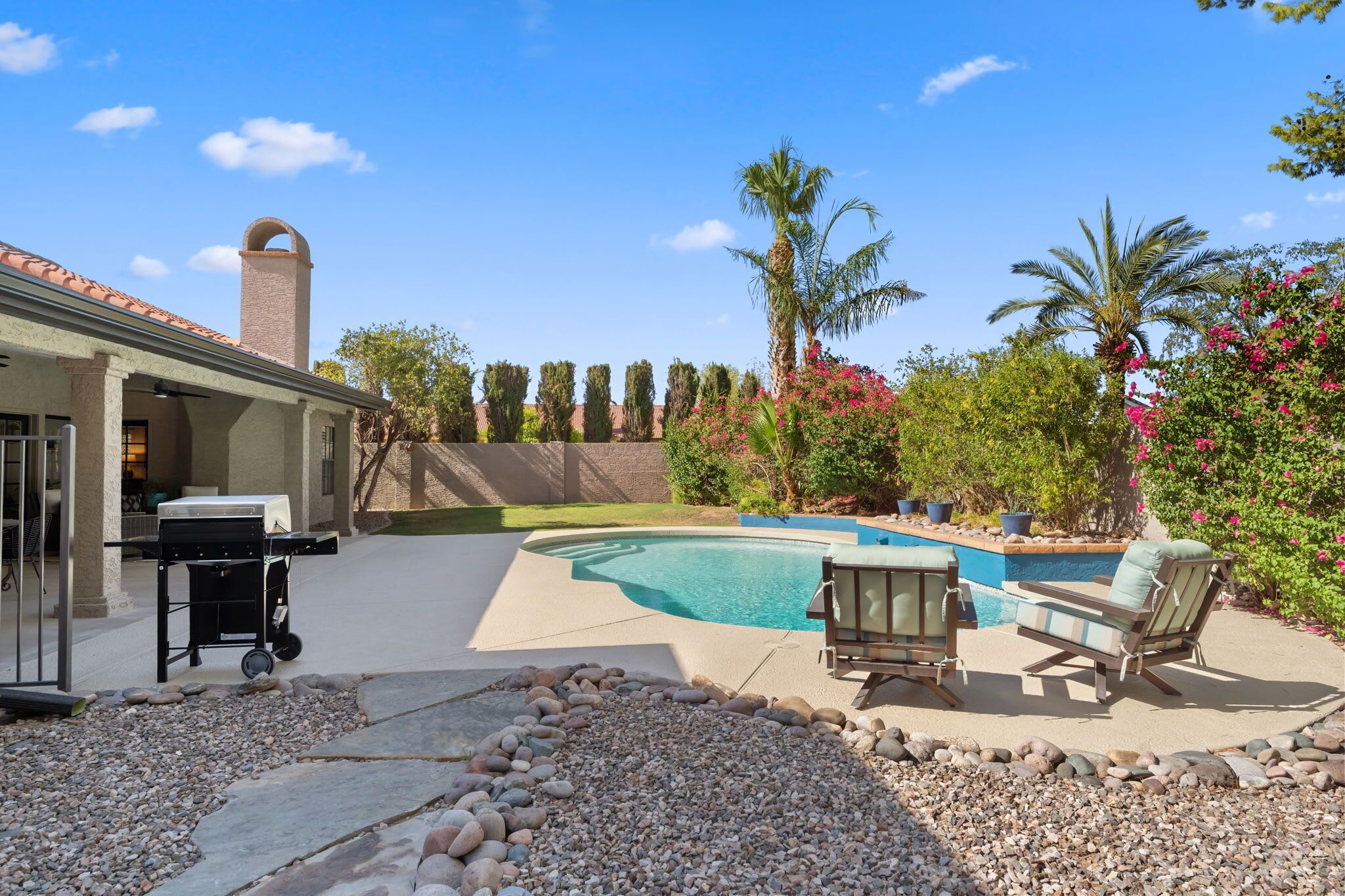 A backyard with a swimming pool, patio furniture, and a barbecue grill.