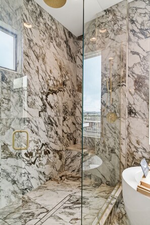 A modern bathroom with marble walls, a glass-enclosed shower, and a white sink. - Elevated Luxury • Amazing Rooftop Views W/Elevator (Nashville)