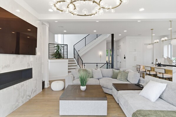 A modern living room with a sectional sofa, a coffee table, a TV mounted on the wall, and a staircase leading to another level. - Elevated Luxury • Amazing Rooftop Views W/Elevator (Nashville)