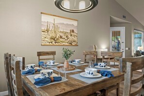 A dining area with a wooden table set for four, blue and white patterned tableware, a cactus painting on the wall, and a wooden chair with a leather seat. - The Retreat at Gold Canyon - Private Pool, Firepit & Superstition Mountain Views (Gold Canyon)