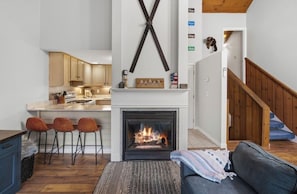 Eine moderne Küche mit Kamin, Holzbarhocker und einer Treppe, die zu einem Schlafzimmer im oberen Bereich führt.