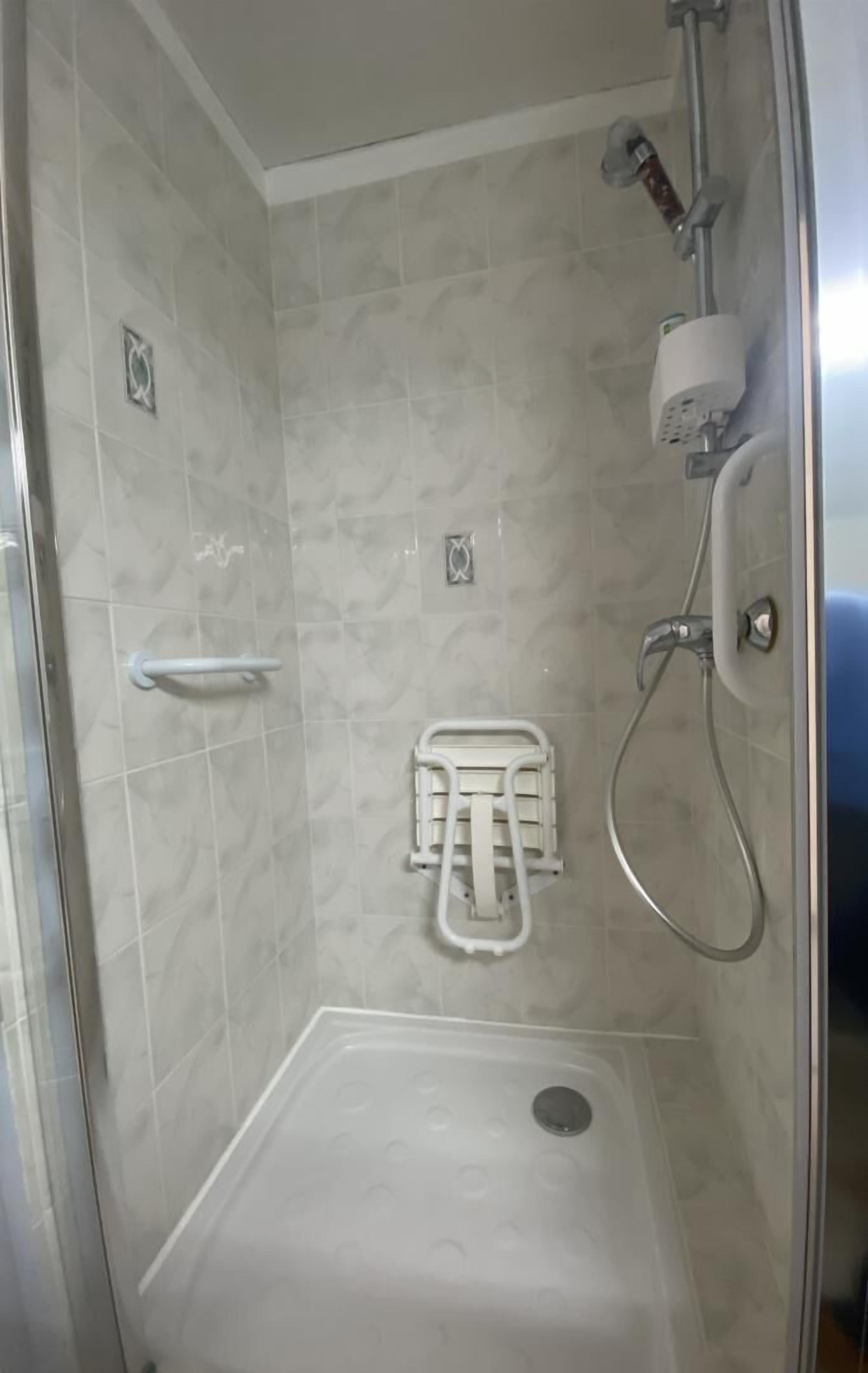 A shower stall with a white seat, a handheld showerhead, and a wall-mounted towel rack.