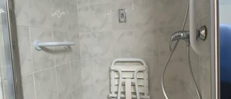 A shower stall with a white seat, a handheld showerhead, and a wall-mounted towel rack.