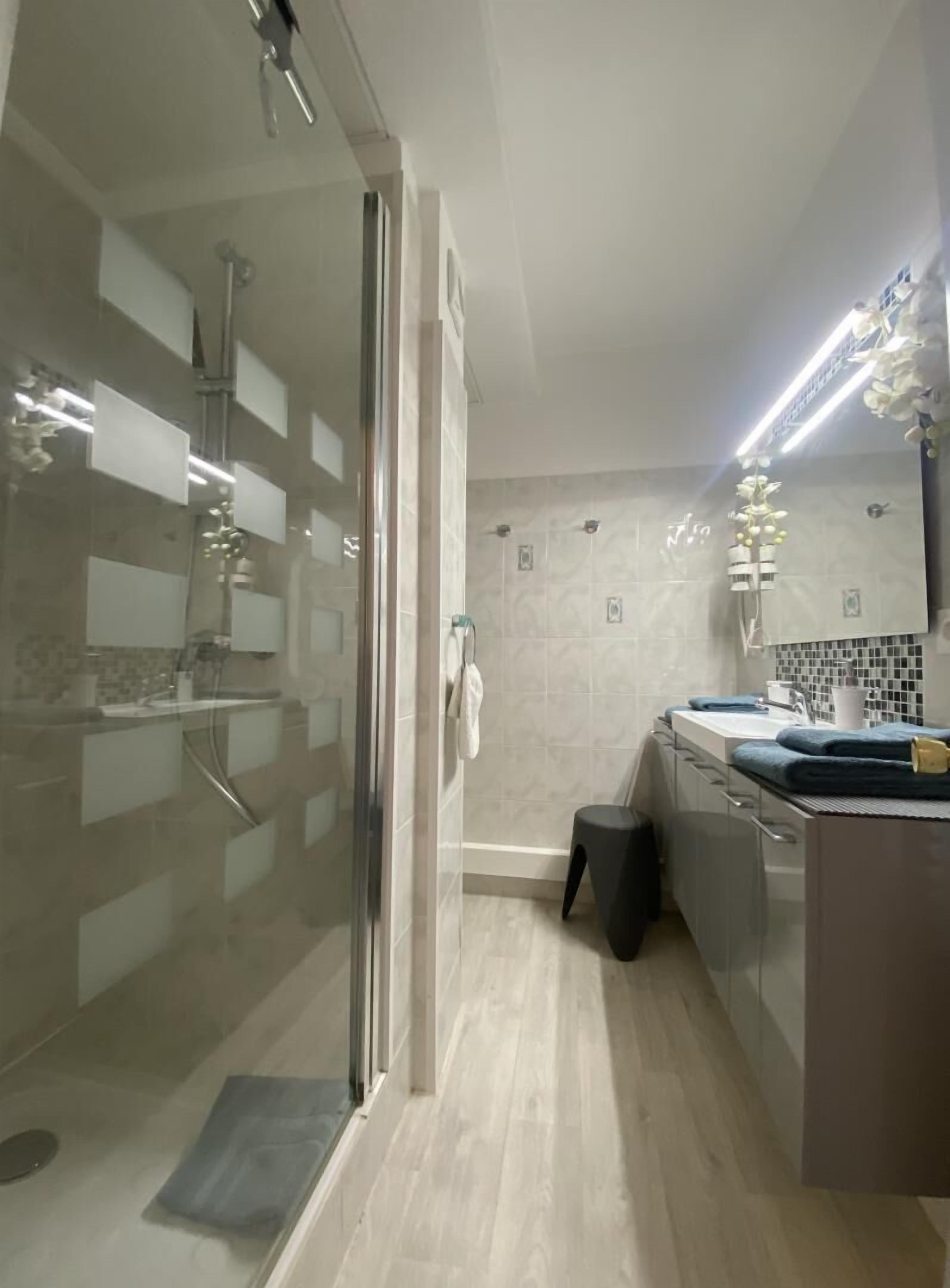Une salle de bain moderne avec une douche à parois de verre, un lavabo avec un miroir et un mur recouvert de carreaux.