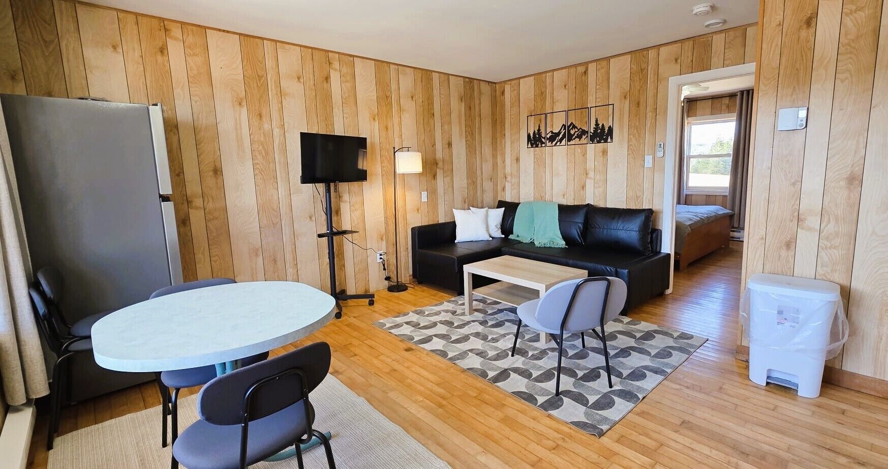 Een kleine leefruimte met een eettafel, stoelen, een bank, een televisie en een kleine prullenbak.