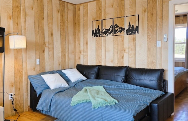 A bedroom with a bed, a wall-mounted artwork, a bedside lamp, and a window.