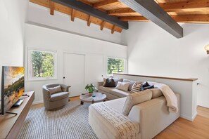 Ein Wohnzimmer mit Sofa, Sessel, Couchtisch, Fernseher und Fenstern.