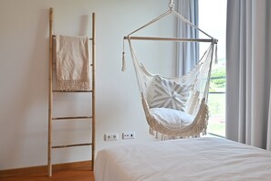 Ein Zimmer mit einem Bett, einem Hängesessel, einer Leiter und Blick ins Freie.