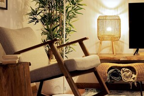 Ein modernes Wohnzimmer mit einem Holzstuhl, einer gewebten Stehlampe, einer großen Topfpflanze und einem Flachbildfernseher.