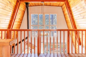 Een houten interieur met een balkon, een raam met uitzicht op bomen en een hanglamp.