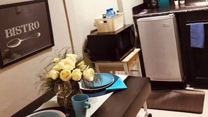 A kitchenette with a microwave, refrigerator, and a small sink. There are two wall clocks, a framed sign with 'BISTRO,' and a vase with flowers on the counter. - Cozy Studio in Santo Domingo Este With Modern Amenities (Santo Domingo Este)