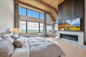 Ein Schlafzimmer mit einem großen Bett, Kamin, Fernseher und Blick auf die Berge.