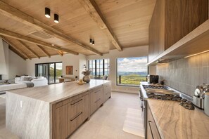 Eine moderne Küche mit einer großen Kochinsel, Holzbalkendecke und Blick ins Freie.