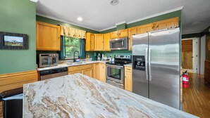 A kitchen with wooden cabinets, stainless steel appliances, a marble countertop, and a green wall. - Mountain Hearth II -Dog friendly! theater room, pool table,arcade,fire pit, 5 min to slopes (Beech Mountain)