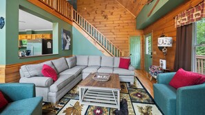A living room with a sectional sofa, a coffee table, and a staircase leading to another level. - Mountain Hearth II -Dog friendly! theater room, pool table,arcade,fire pit, 5 min to slopes (Beech Mountain)