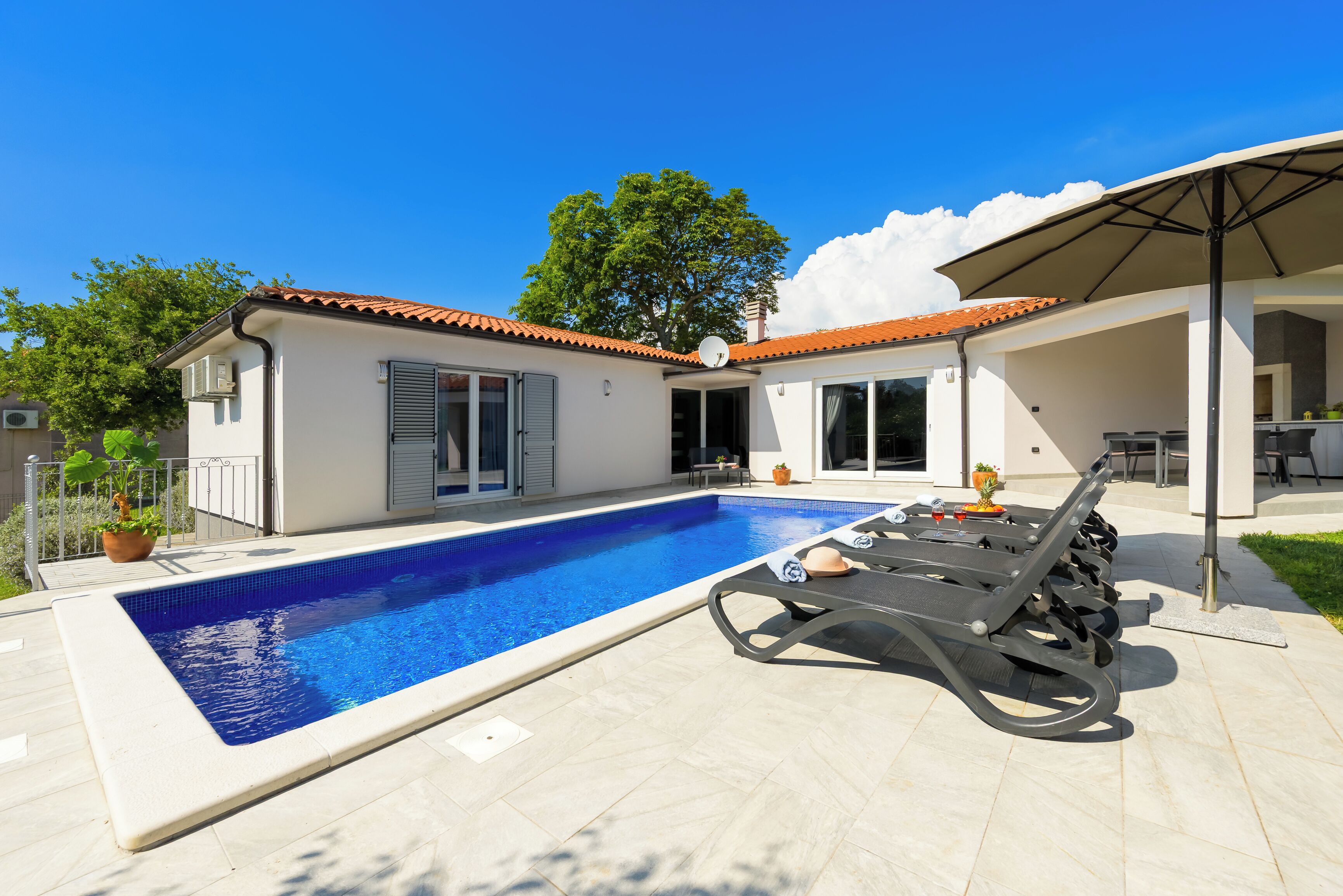 Une piscine avec des chaises longues, un patio couvert et une maison avec un toit en tuiles.