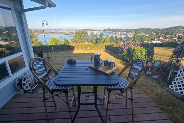 Um pátio com mesa e cadeiras, vista para um lago e uma ponte ao fundo.