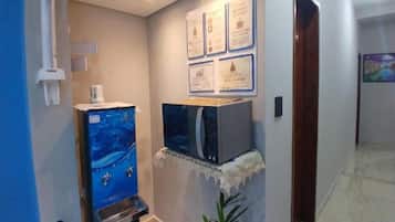 Una habitación con una televisión sobre un soporte, un dispensador de agua y certificados enmarcados en la pared.
