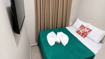 Una habitación de hotel con una cama, un edredón verde, almohadas blancas y una almohada roja con estampado floral.