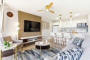 Ein modernes Wohnzimmer mit Flachbildfernseher, einer Couch, einem Couchtisch und einem Essbereich mit Barhocker.