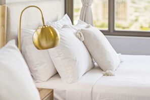 Ein ordentlich bezogenes Bett mit weißer Bettwäsche und einer goldenen Lampe.