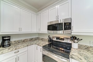 A kitchen with white cabinets, a stainless steel microwave, a stove, and a coffee maker.