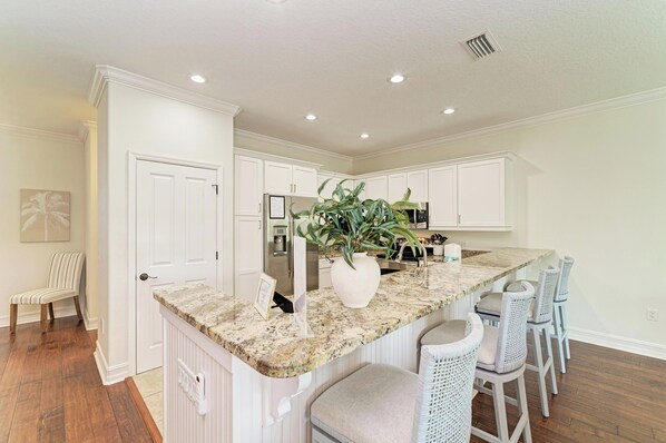 A kitchen with white cabinetry, a granite countertop, and a central island with bar stools. - Still Waters hosted by Beach Retreats FL (Holmes Beach)