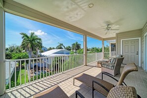 A covered outdoor area with a ceiling fan, a pool, and a view of palm trees and houses.