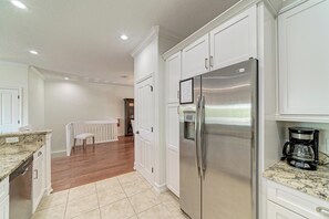 A kitchen with white cabinets, a stainless steel refrigerator, a coffee maker, and a wooden dining table.