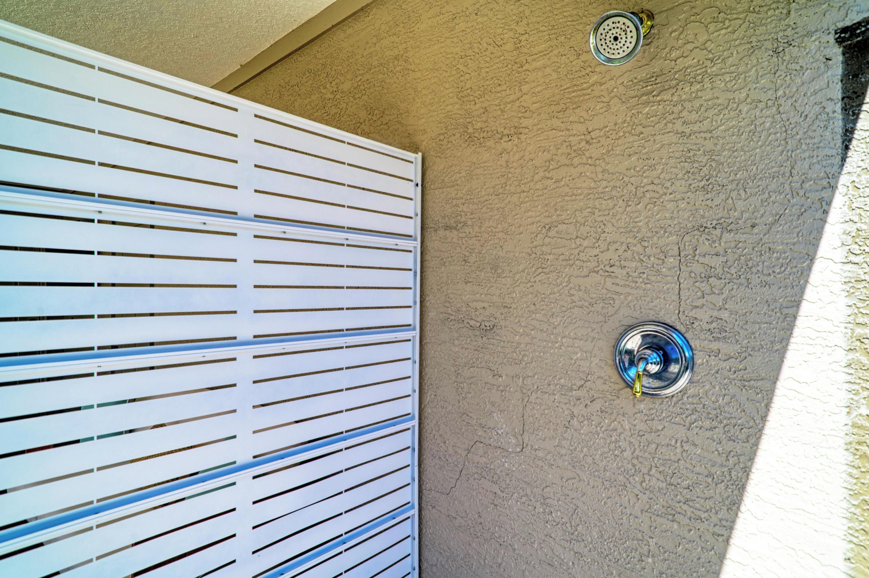 A white exterior wall with horizontal slats and two metallic fixtures, one with a circular design and another with a spout, likely for water.