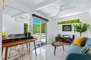 Ein modernes Wohnzimmer mit Sofa, Couchtisch und Sesseln, einer Schiebetür zu einem Außenbereich sowie einem Deckenventilator.