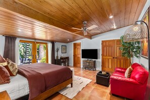 Ein Schlafzimmer mit einem Bett, einem roten Sofa, einem Fernseher, Holztüren und einem Deckenventilator.
