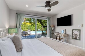 Ein Schlafzimmer mit Bett, Deckenventilator, Fernseher, Schreibtisch mit Stuhl und Blick auf einen Swimmingpool.