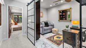 A modern living room with a grey sofa, a coffee table, a bookshelf, and a sliding door leading to another room. - Sol y Soledad: A Modern Palm Springs Retreat with Private Pool, Spa & Office (Palm Springs)