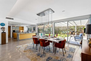 Eine moderne Küche mit Kochinsel, ein Essbereich mit Tisch und Stühlen sowie ein großes Fenster mit Blick auf einen Garten.