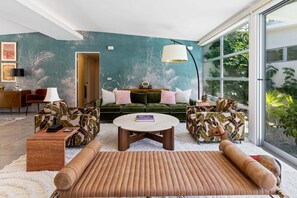 Ein modernes Wohnzimmer mit einer Couch, Sesseln, einem Couchtisch und einem großen Fenster mit Blick auf Grünflächen.