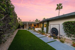 Ein modernes Haus mit gepflegtem Rasen, einem Weg zum Eingang und einer großen, dekorativen Metallskulptur.