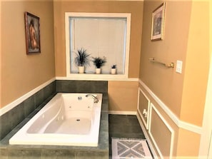 Ein Badezimmer mit einer Badewanne, einem Fenster mit Jalousien und Blumentöpfen auf der Fensterbank.