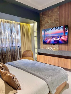 Ein modernes Schlafzimmer mit einem großen Bett, einem an der Wand montierten Fernseher und Blick auf den Ozean.