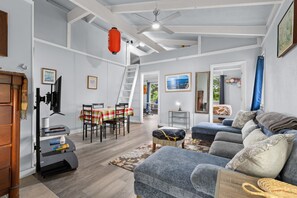 Ein geräumiger Wohnbereich mit einer Couch, einem Esstisch mit Stühlen, einer Treppe und einem Deckenventilator.