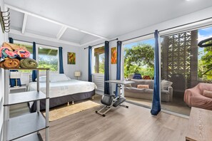 Ein modernes Schlafzimmer mit Bett, Trainingsgeräten, Schreibtisch und Balkon mit Blick auf Grünflächen.