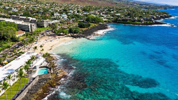An aerial view of a coastal resort with a beach, clear blue waters, and a mountainous backdrop. - Hilo 2BR Home with AC | Near Beaches & Downtown (Hilo)