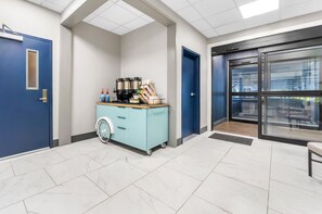 En lys, moderne lobby med en blå dør, en lille serveringsvogn med drikkevarer og en glas elevator.