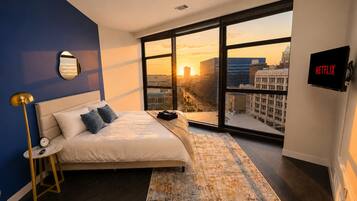 Habitación de hotel moderna con una cama grande, vistas de la ciudad, un televisor de pantalla plana y un espejo de pared original.