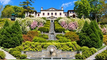 Un edificio grande y señorial con un jardín formal, que incluye una fuente y setos bien cuidados.