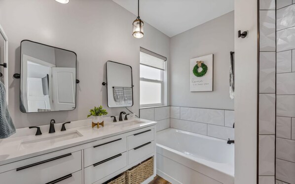 A modern bathroom with a white vanity, a large mirror, a window, a bathtub, and a wall-mounted light fixture. - Modern Home Escape in the Pines - Family Friendly (Show Low)
