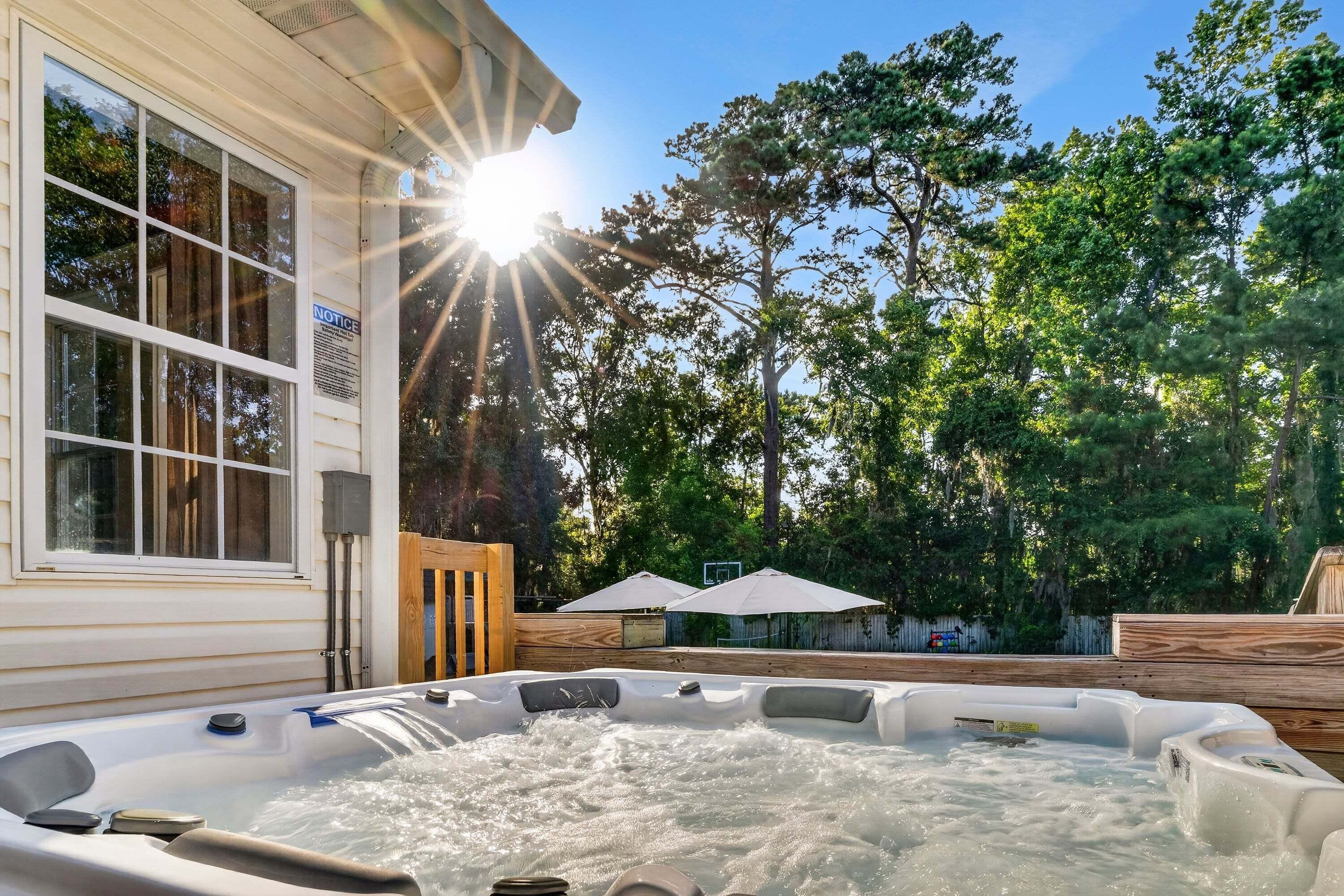 Un bain à remous avec de l’eau en circulation, une terrasse en bois et un bâtiment doté de grandes fenêtres.