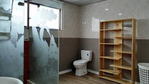 Een badkamer met een douchecabine van glas, een toilet, een houten kastje en een witte wasmand.